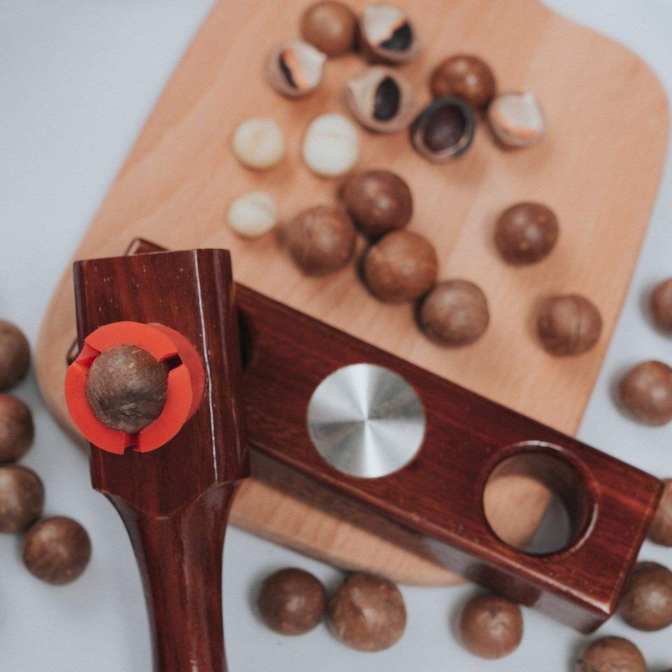 MaccaWakka macadamia nut cracker with a macadamia held in the red silicone cup, on a timber chopping board with cracked nuts